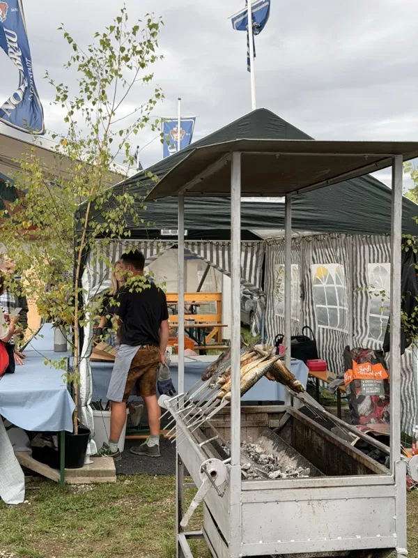 Der Steckerlfischstand mit Zeltdach und Grill auf einem Volksfestplatz